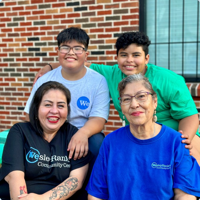 Two staff members and two youth participants smiling together outside the community center.